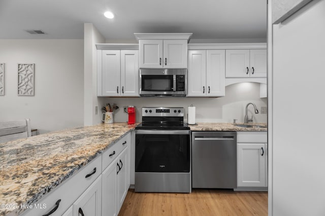 kitchen with light stone counters, visible vents, a sink, light wood-style floors, and appliances with stainless steel finishes