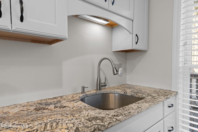 kitchen featuring white cabinetry, light stone countertops, and a sink