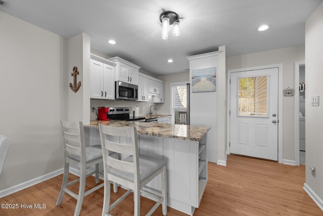 kitchen featuring a peninsula, light stone counters, appliances with stainless steel finishes, and light wood finished floors