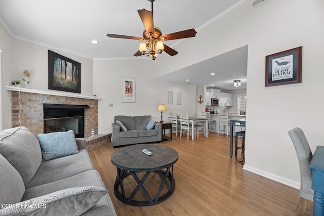 living room with baseboards, recessed lighting, a fireplace, crown molding, and light wood-type flooring