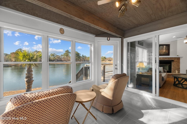 sunroom / solarium featuring a brick fireplace, a ceiling fan, and a water view