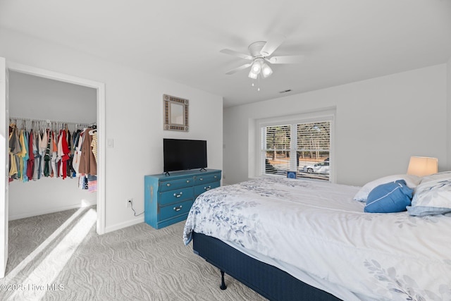 bedroom with a spacious closet, visible vents, light colored carpet, a closet, and a ceiling fan