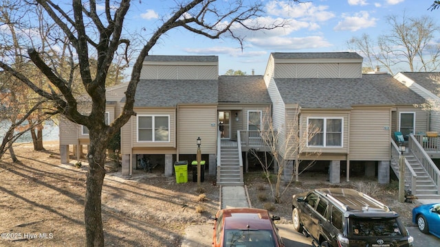 back of house featuring stairway and roof with shingles