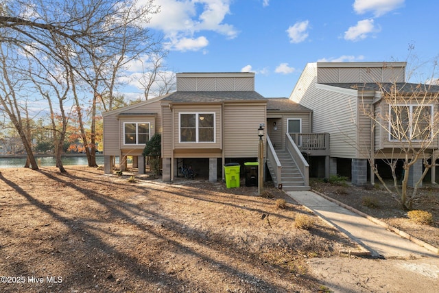 view of front of property with stairway, a water view, and a shingled roof