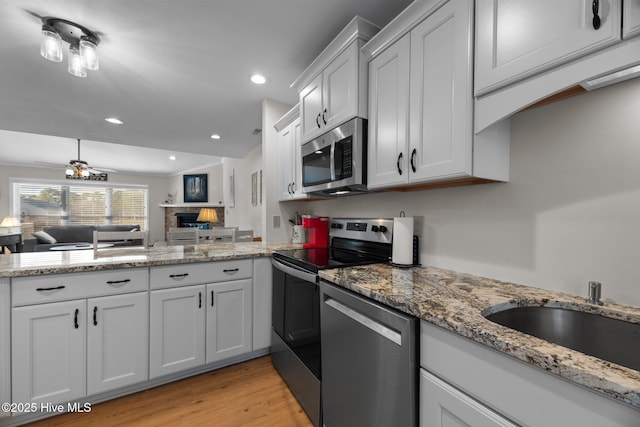 kitchen featuring open floor plan, a peninsula, light wood-style floors, stainless steel appliances, and a sink