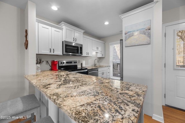 kitchen with a sink, light stone counters, white cabinetry, stainless steel appliances, and a peninsula