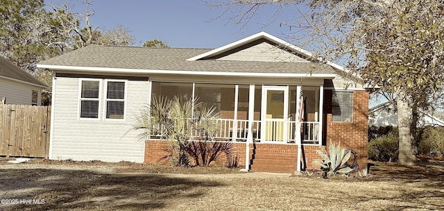 view of front of house with fence, roof with shingles, and a sunroom