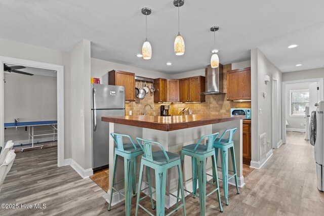 151 NE 9th St, Oak Island, NC 28465 - kitchen featuring freestanding refrigerator, wall chimney range hood, butcher block countertops, brown cabinetry, and baseboards