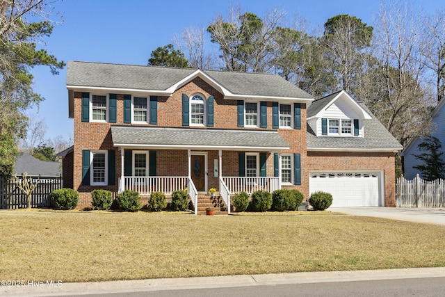 colonial home with a shingled roof, covered porch, concrete driveway, a front yard, and fence