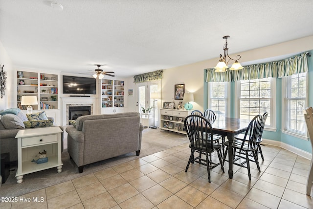 dining space with a ceiling fan, a brick fireplace, light tile patterned flooring, a textured ceiling, and baseboards