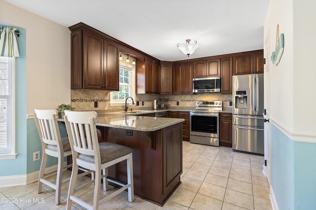 kitchen with light tile patterned floors, appliances with stainless steel finishes, light stone countertops, a peninsula, and a kitchen bar