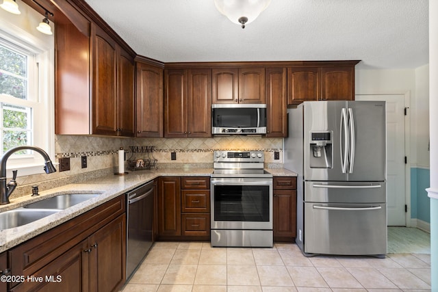 kitchen with light tile patterned floors, appliances with stainless steel finishes, backsplash, and a sink