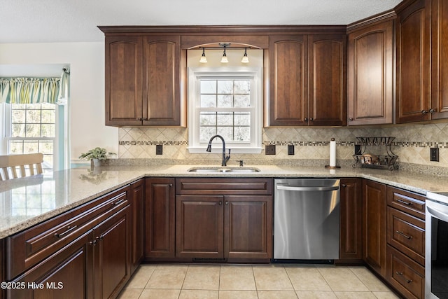 kitchen with light tile patterned floors, tasteful backsplash, appliances with stainless steel finishes, a sink, and light stone countertops