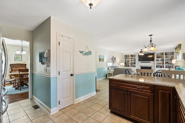 kitchen featuring light tile patterned floors, ceiling fan with notable chandelier, a fireplace, open floor plan, and decorative light fixtures