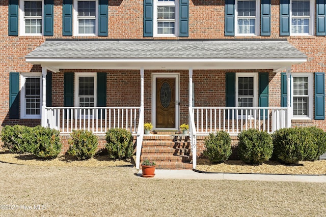 property entrance with covered porch, brick siding, and roof with shingles