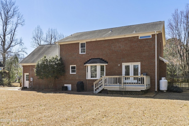 rear view of house with brick siding, a lawn, a deck, and fence