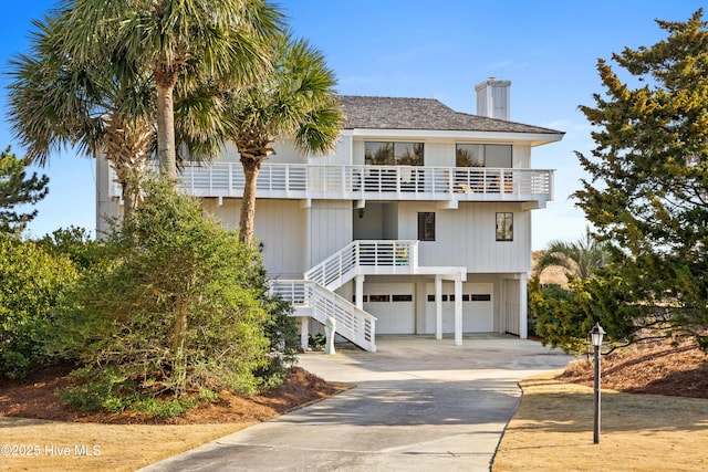 exterior space with a chimney, a balcony, a garage, driveway, and stairs