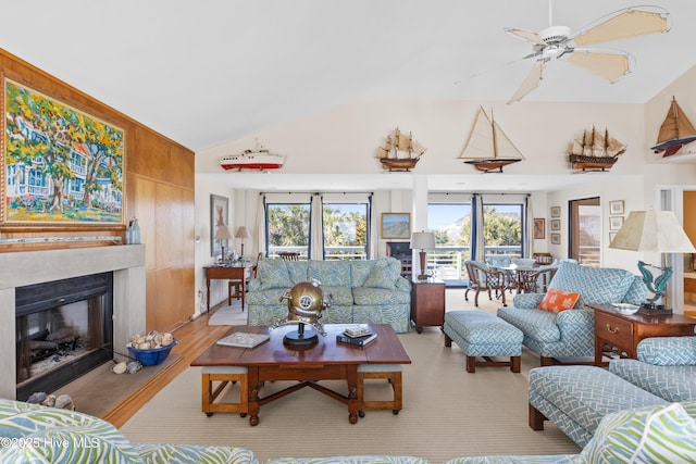 living area with vaulted ceiling, a glass covered fireplace, light wood-style flooring, and a ceiling fan