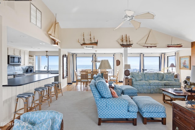 living area with ceiling fan, high vaulted ceiling, light wood-style flooring, and a wealth of natural light