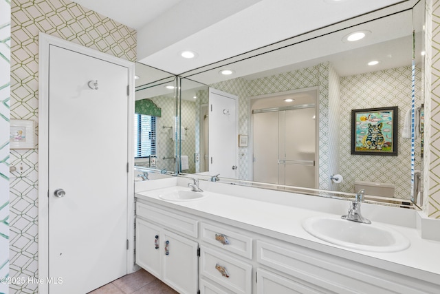 bathroom with double vanity, a sink, toilet, and wallpapered walls