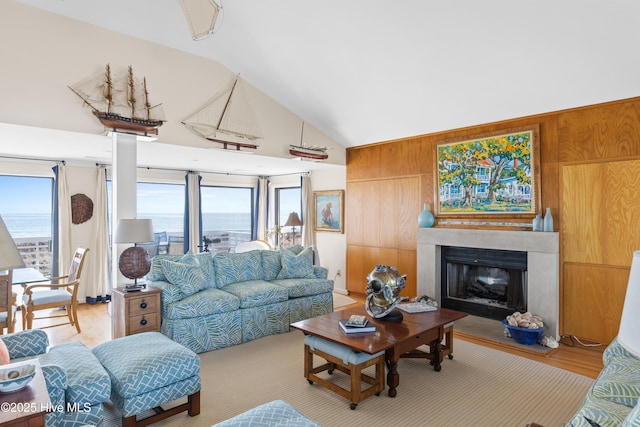 living area featuring wooden walls, high vaulted ceiling, wood finished floors, and a glass covered fireplace