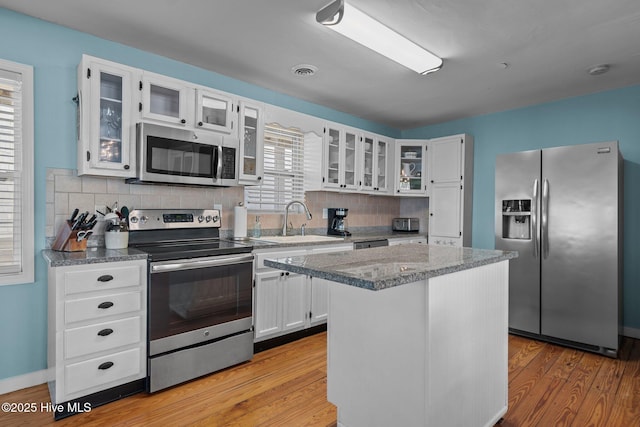 kitchen featuring decorative backsplash, light wood-type flooring, a sink, stainless steel appliances, and white cabinetry