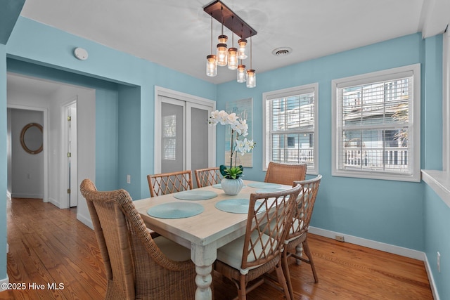 dining space featuring a notable chandelier, light wood-style flooring, visible vents, and baseboards