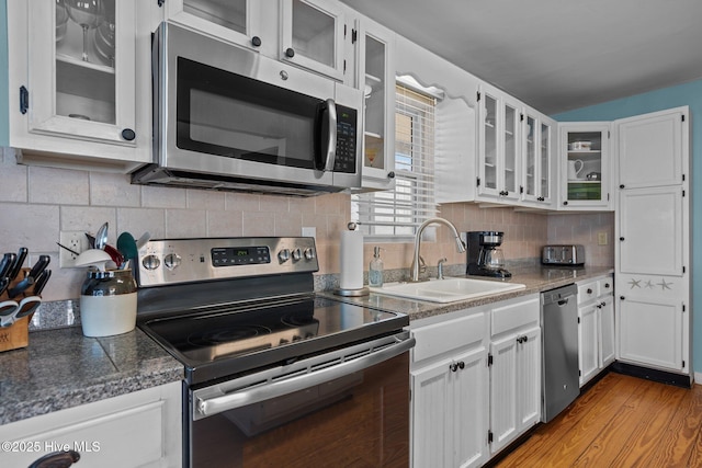 kitchen featuring glass insert cabinets, white cabinetry, a sink, light wood-style flooring, and stainless steel appliances