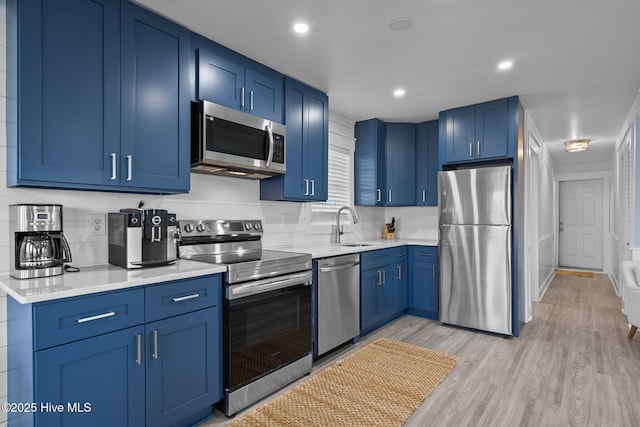 kitchen featuring blue cabinetry, appliances with stainless steel finishes, light wood finished floors, and light countertops