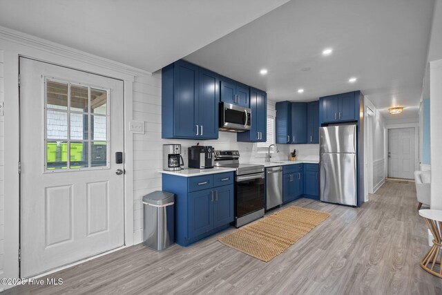 kitchen featuring appliances with stainless steel finishes, light wood-type flooring, a sink, and blue cabinetry