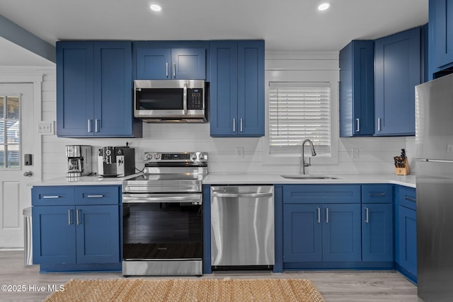 kitchen with blue cabinetry, stainless steel appliances, light countertops, decorative backsplash, and a sink