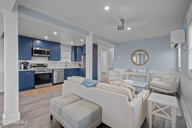 living area with ceiling fan, a wall unit AC, light wood-style flooring, recessed lighting, and wainscoting