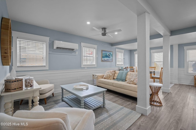 living room featuring a wainscoted wall, ceiling fan, a wall unit AC, and wood finished floors