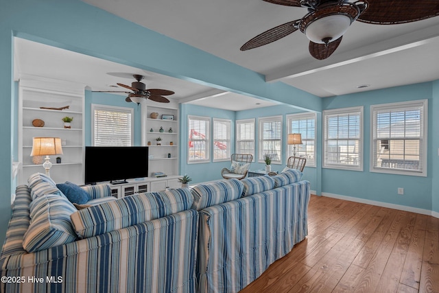 living room with ceiling fan, hardwood / wood-style flooring, built in features, baseboards, and beam ceiling