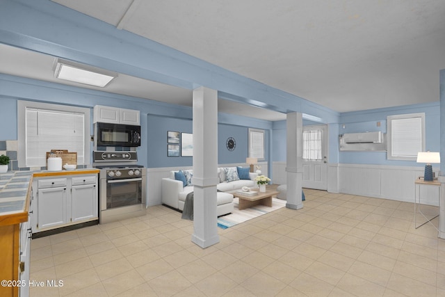 kitchen with black microwave, tile countertops, white cabinetry, wainscoting, and stainless steel range with gas cooktop