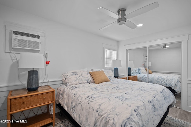 bedroom featuring a closet, a ceiling fan, wood finished floors, and a wall mounted air conditioner
