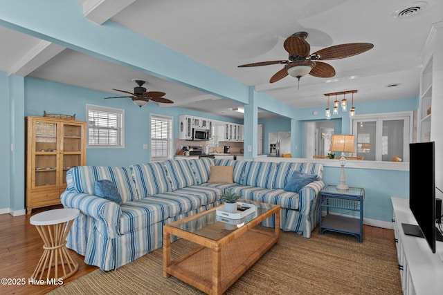 living area featuring wood finished floors, a ceiling fan, visible vents, baseboards, and beam ceiling