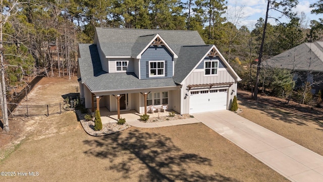 view of front of house with a shingled roof, concrete driveway, covered porch, board and batten siding, and fence