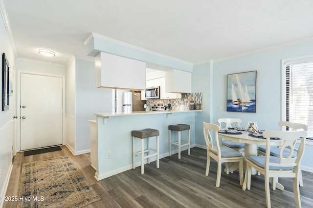 kitchen featuring white cabinets, dark wood finished floors, a kitchen breakfast bar, stainless steel appliances, and backsplash