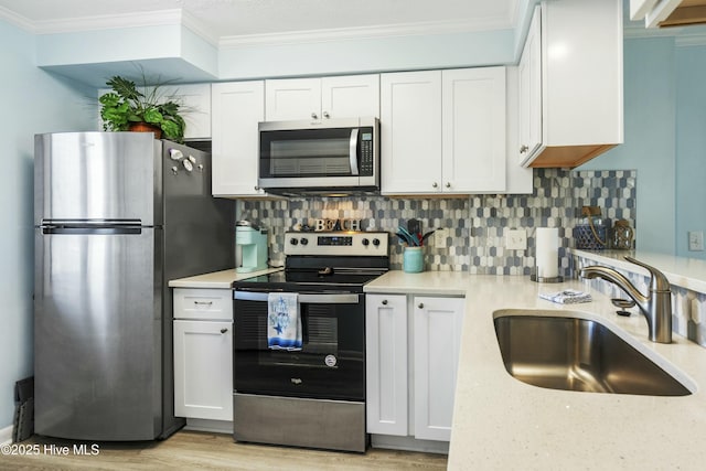 kitchen featuring a sink, white cabinets, appliances with stainless steel finishes, tasteful backsplash, and crown molding