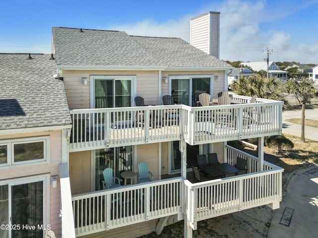 rear view of property with a shingled roof, a chimney, and a wooden deck