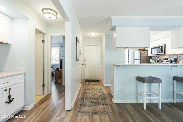 kitchen featuring a breakfast bar area, dark wood-style flooring, white cabinets, appliances with stainless steel finishes, and tasteful backsplash