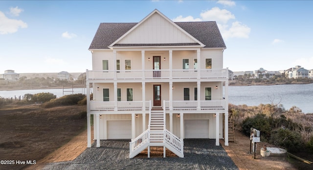 coastal inspired home with stairway, an attached garage, gravel driveway, a balcony, and board and batten siding