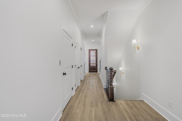 hallway with light wood-style floors, baseboards, crown molding, and an upstairs landing