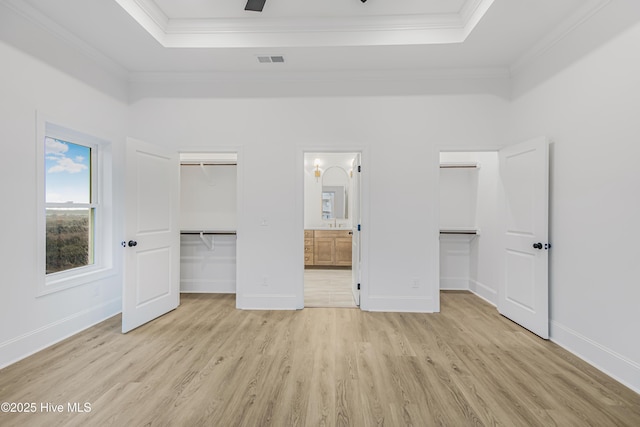 unfurnished bedroom featuring a walk in closet, a closet, crown molding, and a tray ceiling