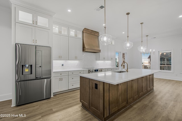 kitchen with visible vents, backsplash, a sink, stainless steel fridge, and premium range hood