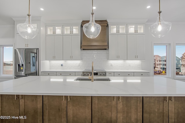 kitchen featuring ornamental molding, stainless steel refrigerator with ice dispenser, a sink, and a large island with sink