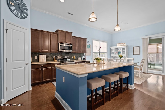 kitchen with visible vents, dark wood finished floors, stainless steel appliances, a kitchen bar, and backsplash