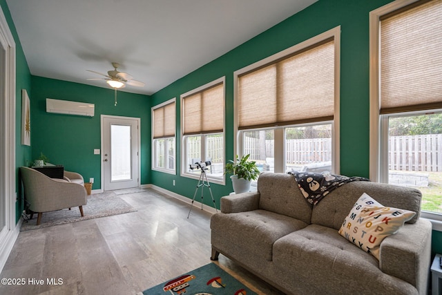 living room with ceiling fan, an AC wall unit, wood finished floors, and baseboards