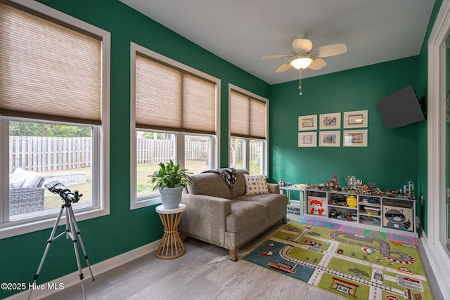 playroom with a ceiling fan, plenty of natural light, baseboards, and wood finished floors